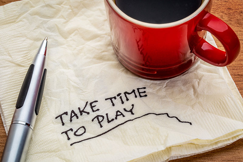 A cup of coffee on a napkin, on which is written "Take Time to Play".