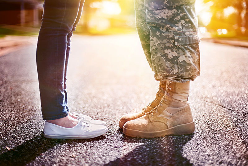 The feet of a soldier and his wife with the sun shining in the background.