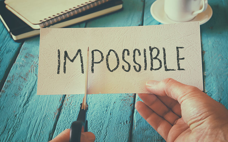 A piece of paper with the word "impossible" with the "im" being cut off by a pair of scissors.