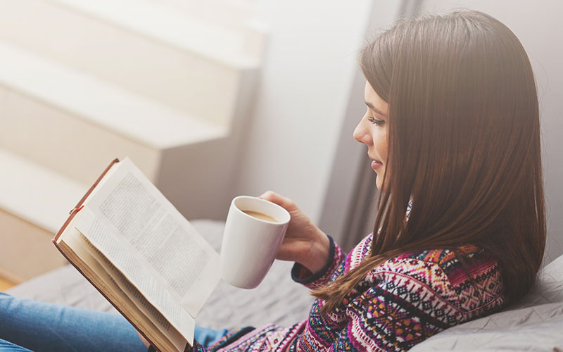 Woman on the couch with a cup of coffee reading a book.
