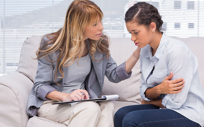 A female therapist sitting on the couch comforting a female client.