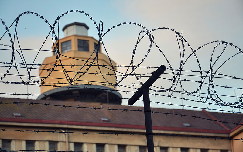 View of a prison surrounded by barbed wire with a blue sky behind.