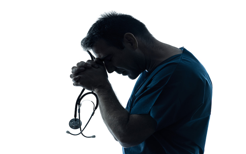 Man holding his head on his hands like he was praying while holding a stethoscope